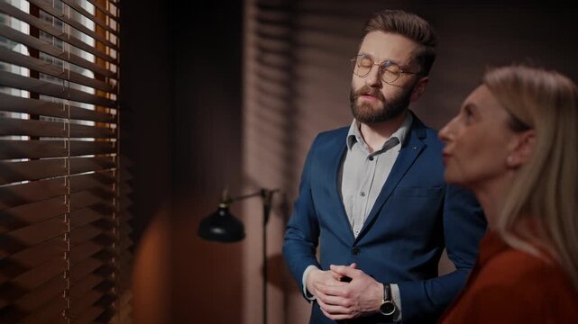 Male casting manager conducting audition for role in movie. Man casting director having discussion with actress. Woman auditioning for film role. Man in suit talking to woman in dim room.