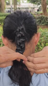 Close up of female hands carefully braiding thick black hair outdoors, 20 seconds footage