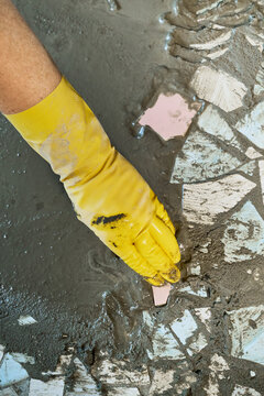 Worker hand wearing yellow glove arranging broken ceramic tiles for DIY mosaic art project. Upcycling old materials