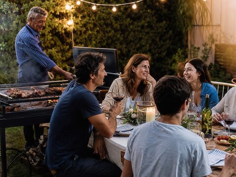 Argentinische Familie und Freunde feiern Silvester bei einem traditionellen Asado im sommerlichen Garten, genie&szlig;en gegrilltes Fleisch, Rotwein und geselliges Beisammensein.