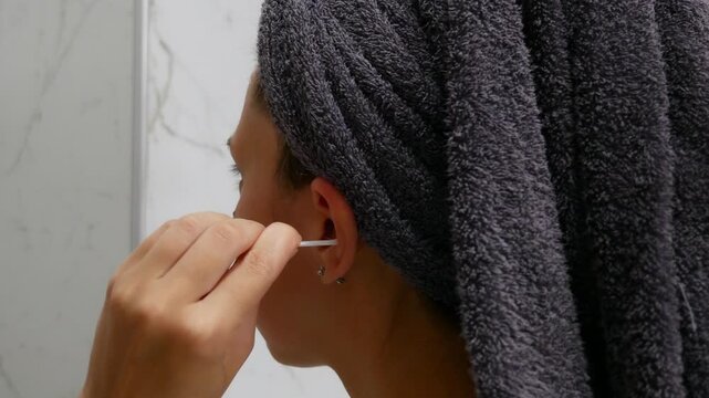 Close-up of woman cleaning outer ear with cotton swab during daily hygiene routine.