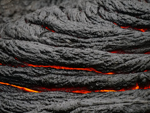 Glowing red molten lava cooling into black basalt rock crust in Iceland