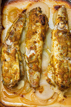 Baked fish fillets seasoned with spices and herbs, placed on a bed of sliced onions in a rectangular baking dish, ready for serving