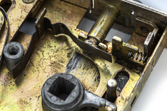 Detailed macro photograph of an old vintage brass door lock mechanism revealing intricate internal components including worn metal levers springs square spindle socket and aged patina surfaces