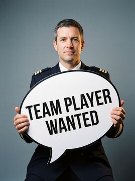 Confident middle aged pilot in uniform holds a speech bubble sign reading team player wanted