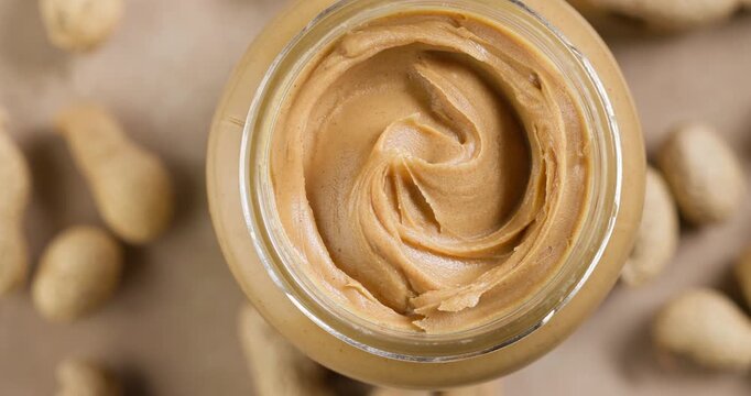 Open Jar of Peanut Butter Rotating on Warm Beige Background, Top View