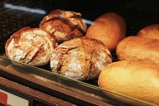 Fresh rustic artisan bread loaves displayed behind glass in bakery. Golden crust and flour texture on traditional baked products. Food retail counter with daily bakery assortment and fresh bread.