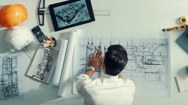 Top view of smart civil engineer drawing and measuring blueprint by using ruler. Aerial view of architect scatch building project plan at meeting table with equipment and safety helmet. Alimentation.