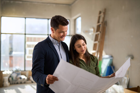 Happy young couple examining blueprints together during their new apartment renovation.