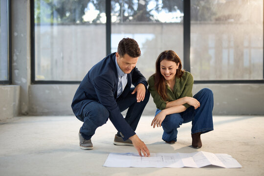 Young happy couple talking while analyzing housing plans at construction site.