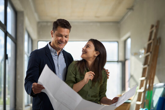 Happy young couple talking while examining blueprints together during their new apartment renovation.