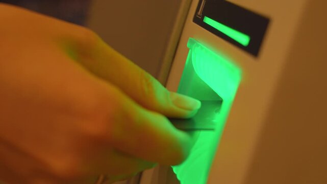 Close up view of a hand inserting a credit card into an atm reader with a flashing green light, showing the process of making a financial transaction or withdrawing cash from the machine