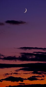 Crescent moon in purple twilight sky with dark clouds at sunset
