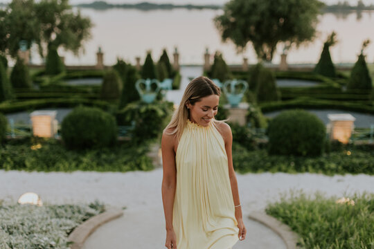 Woman walks through garden near water at dusk with green plants and trees