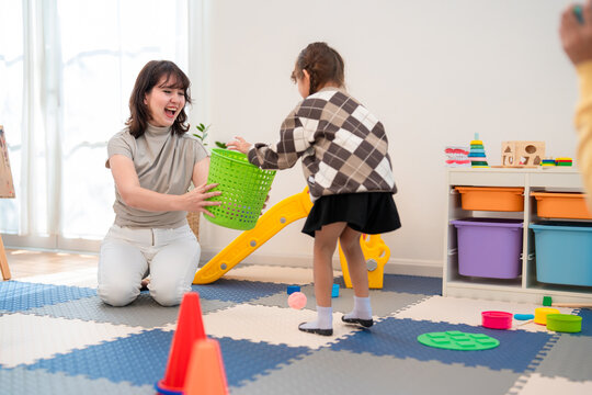 Child plays with toys in playroom while adult helps her pick up items from the floor at a home in the daytime