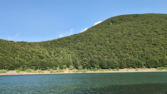Mountain lake with gentle water ripples surrounded by green beech forest in the Apennines, Italy
