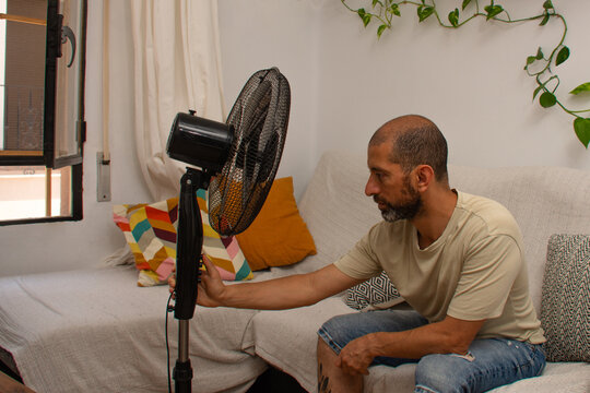 Hispanic man trying to turn on fan during extreme summer heatwave at home