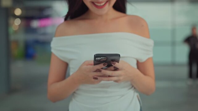 Close up of happy Asian woman typing text message on smartphone while walking indoors, smiling female using mobile phone for chatting and online shopping at shopping mall, connection, technology
