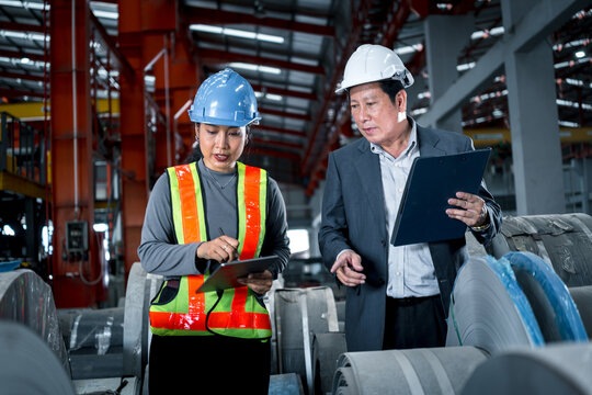 two professional engineer, worker, technician use clipboard discuss work, walk in steel metal manufacture factory plant industry. engineering man and woman wear hard hat check quality machine