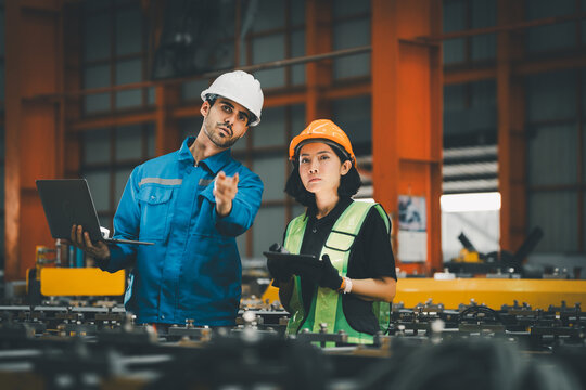 two professional engineer, worker, technician use clipboard discuss work, walk in steel metal manufacture factory plant industry. engineering man and woman wear hard hat check quality machine