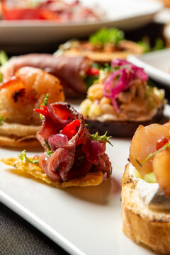 Selection of gourmet Spanish tapas and pintxos served on a white plate, featuring seafood, cured meats, and fresh toppings.