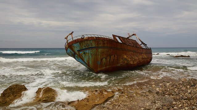Agios Gordios, bad weather, cloudy sky, shipwreck, graffiti painting, surf, wide angle close-up, in the foreground rocky coastline and onrushing sea, wreck from diagonal below, rusty, colourfully painted, Corfu Island, Ionian Islands, Greece