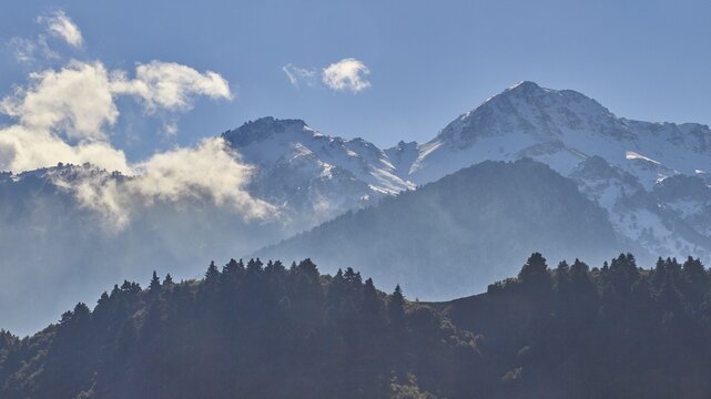 Snow-capped mountain peaks rise behind wooded hills under a blue sky, Erymanthos Mountains, north-west of the Peloponnese peninsula, Peloponnese, Greece