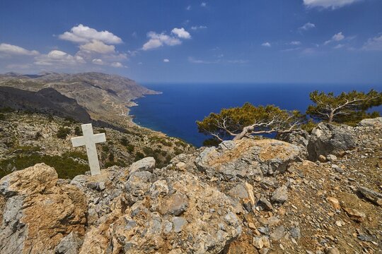 Rugged south coast, wayside cross, windswept trees, rocks, blue sky, white clouds, wide angle shot, Asterousia mountains, central Crete, south coast, Crete, Greece