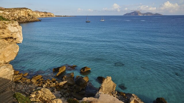Rocky coast, sailing boats, Levanzo Island, Scogliera di Cala Rossa, Cala Rossa, Favignana, Egadi Islands, Sicily, Italy