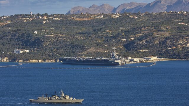 Aircraft carrier USS Gerald R. Ford, largest aircraft carrier in the world, anchored in Souda Bay on February 24, 2026, Greek Navy S-class frigate Kountouriotis, military ship and coastal strip with mountains in the background, US Navy, Souda Bay, Akrotiri Peninsula, Chania Province, Crete, Greek Islands, Greece