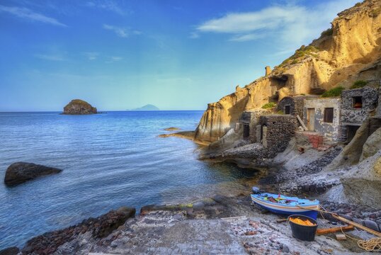 Pollara Bay, Salina island, stone coastline with small buildings and a boat on the shore, surrounded by clear sea, UNESCO World Heritage Site, Aeolian Islands, Aeolian Islands, Sicily, Italy