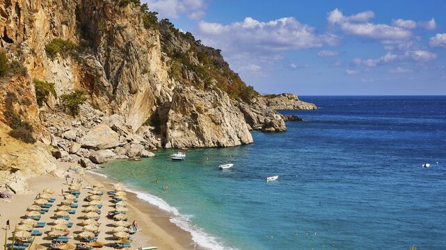 An idyllic beach with blue water and boats, framed by rocks and parasols in sunny weather, Kyra Panagia, Kyra Panagia Beach, East Coast, Karpathos, Dodecanese, Greek Islands, Greece
