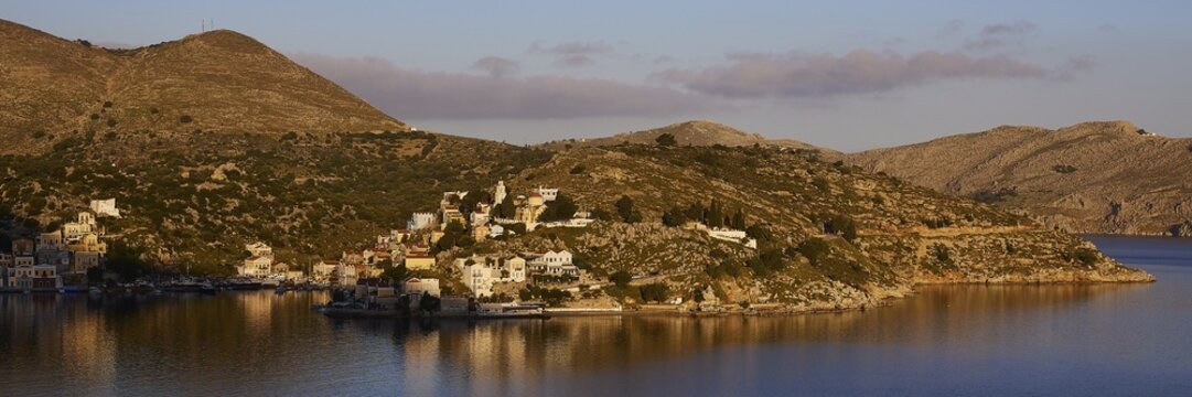 Island in a quiet bay, framed by mountains and bright sky in the morning light, Symi Town, Symi, Dodecanese, Greek Islands, Greece