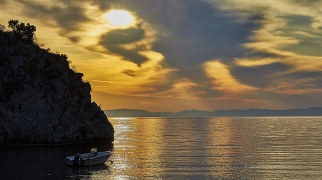 Atmospheric sunrise over the sea with cliffs and a boat, Mani Peninsula, Peloponnese, Greece
