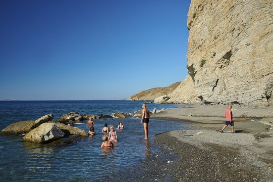 People enjoying the sea on a rocky beach under a clear blue sky, Embros Thermae, Kos, Dodecanese, Greek Islands, Greece