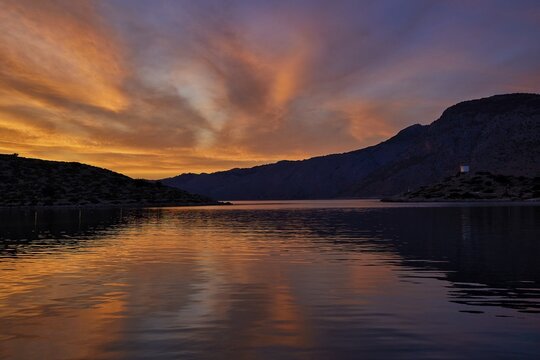 Colourful sunset over a calm lake with mountainous backdrop, Holy Week, Bay of Panormitis, Panormitis Monastery, Symi, Dodecanese, Greek Islands, Greece