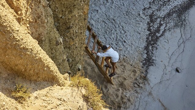 Tourist descending ladder, rocky cove, colourful lava rocks, Tsigrado Beach, Milos Island, Cyclades, Greece