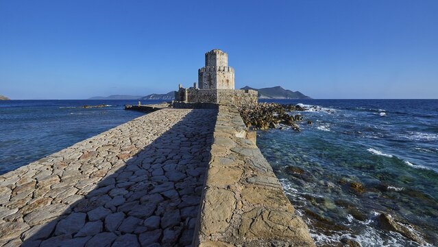 Stone path leads to a castle by the sea under a bright blue sky, octagonal medieval tower. Islet of Bourtzi, sea fortress of Methoni, Peloponnese, Greece