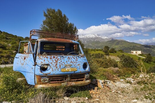 Abandoned rusty blue car on a green field with mountains in the background, wrecked vehicle, Crete, Greek Islands, Greece