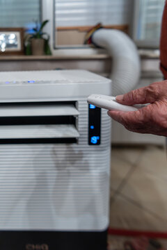Senior using remote control to adjust portable air conditioner in residential home