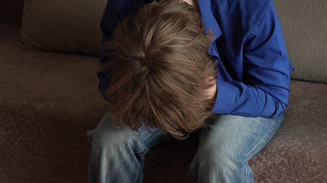 Young man (zoomer) with messy hair leaning forward
 and holding his head. Visibly troubled, feeling stress, burnout and mental exhaustion. Depression and mental health concept.