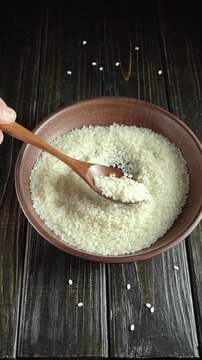 Hand scooping white rice from a wooden bowl with a spoon, showcasing the gradual movement of grains in a rustic kitchen setting