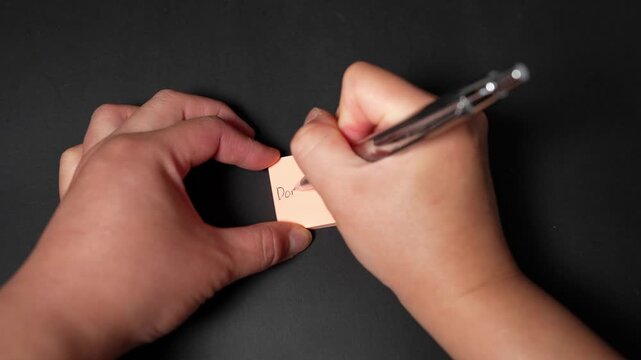Close up of woman&rsquo;s hands writing a reminder note to drink water on small sticky pad
