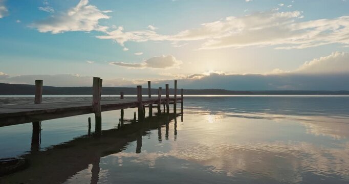 Wooden jetty pier on calm lake at sunset with clouds reflection in the ripple water