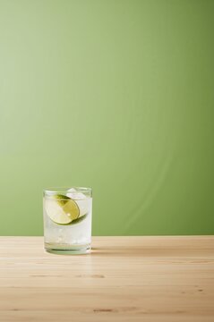 Caipirinha cocktail with fresh lime and ice in glass on wooden table against green background 