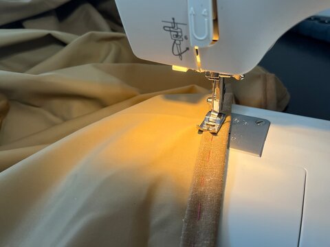 Close-up of a sewing machine foot shortening a mustard yellow curtain fabric. Professional or DIY home decor alteration process, stitching a neat hem on drapes using a sewing needle and thread.
