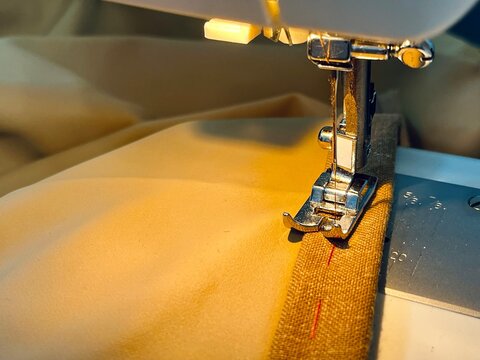 Tailoring and adjusting curtain length by sewing a new hem. Close-up video or photo of a sewing machine needle pierce-stitching thick golden-yellow window curtains.