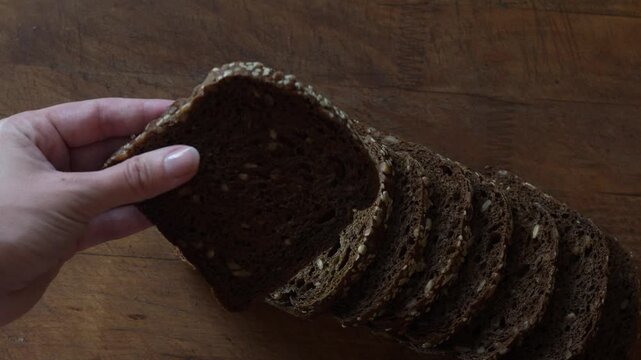 Hand takes slice of cereal sourdough rye bread close up. Detailed texture of healthy wholegrain bread rich of fiber, healthy eating concept.