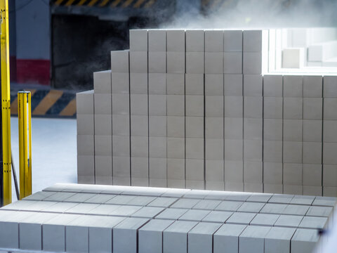 Massive, neatly arranged stacks of freshly manufactured white silicate bricks emit steam inside an industrial production facility.