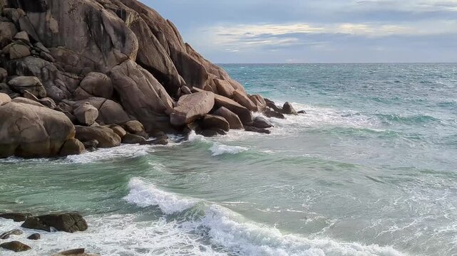 Static shot of rocky coastline with waves breaking and crashing on shore under overcast sky at sea